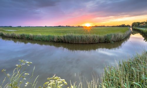 Wide angle landscape over river bend at sunset in flat agricultural landscape in Groningen the Netherlands